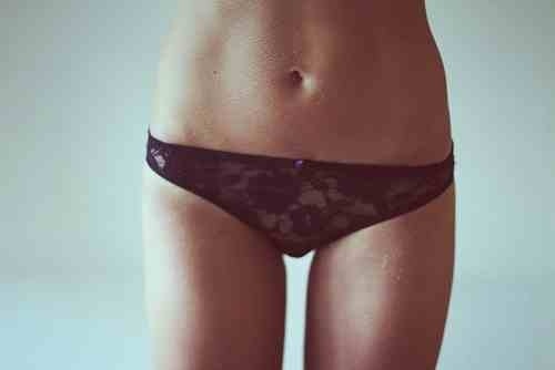 A female torso in black lace panties. she has pale skin and a flat stomach on a pale blue duck egg colour background