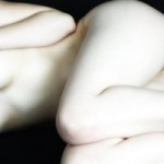 A naked torso of a woman in black and white she is curled into the fetal position. all that is visible is her right arm and her legs. It is suggestive but displays no nudity